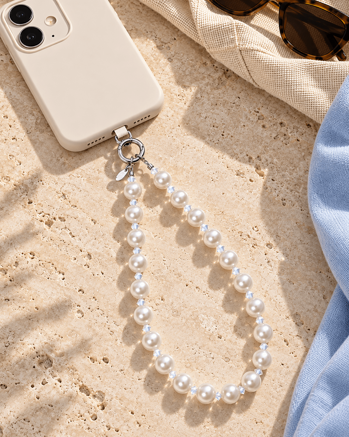 White pearl and clear crystal phone chain attached to an ivory phone on a light stone surface.