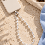 White pearl and clear crystal phone chain attached to an ivory phone on a light stone surface.