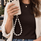 Woman in a cream jacket holding an ivory phone with a white pearl and clear crystal phone chain.