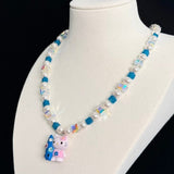 Angled view of a blue crystal and pearl necklace with a colorful cat charm on a white jewelry bust against a black background.